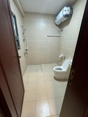 A small, tiled bathroom with a toilet, a hand dryer, and a wall-mounted air conditioning unit. - Pyramids Hotel (Seeb)