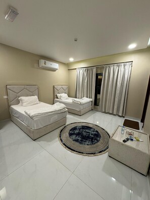 A hotel room with two beds, a round rug, a coffee table, and an air conditioning unit. - Pyramids Hotel (Seeb)
