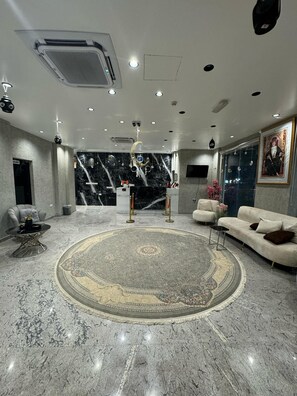 A lobby with a marble floor, a reception desk, sofas, and a large rug. - Pyramids Hotel (Seeb)