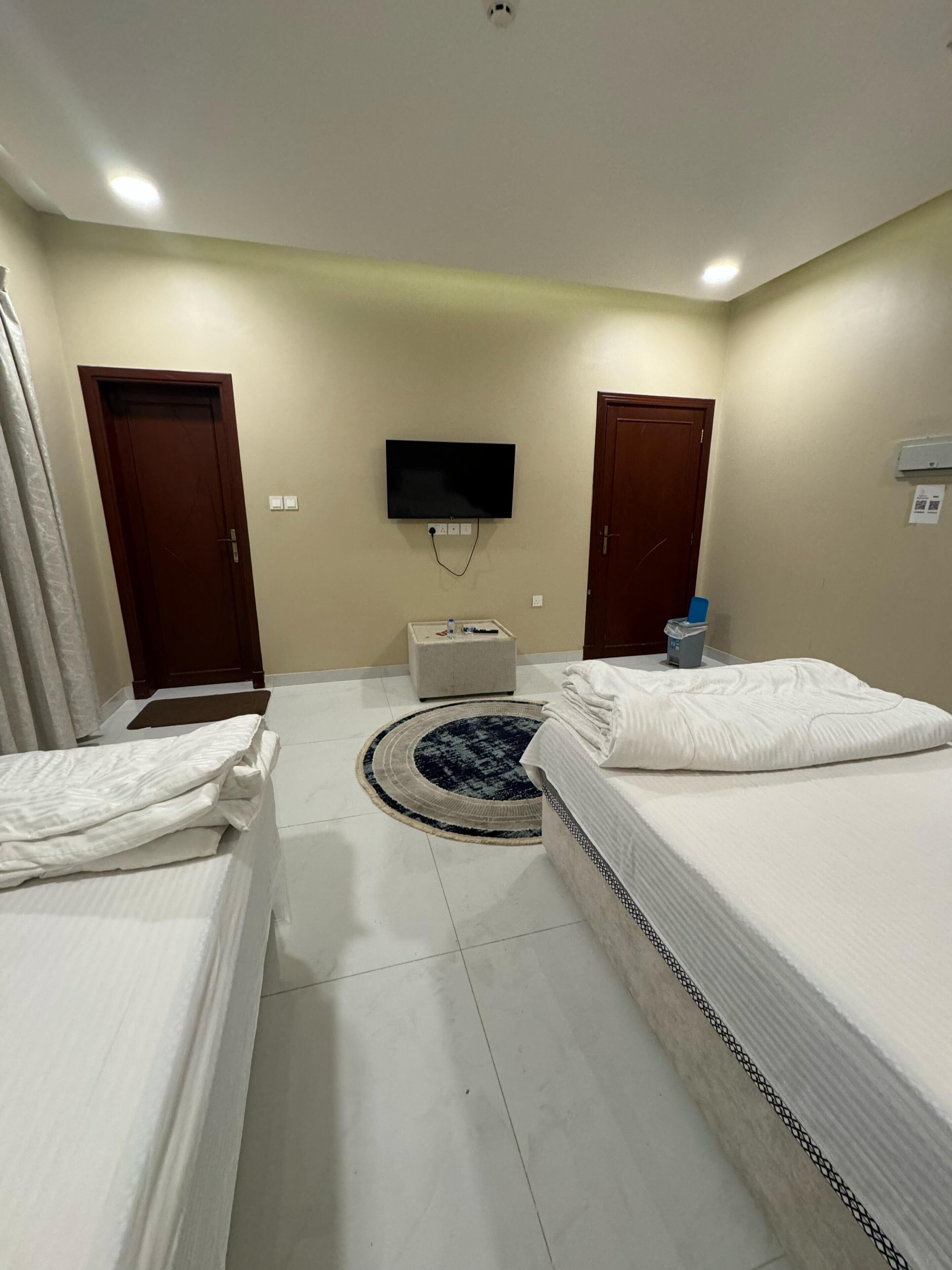 A hotel room with two beds, a TV mounted on the wall, a small table, and a door.