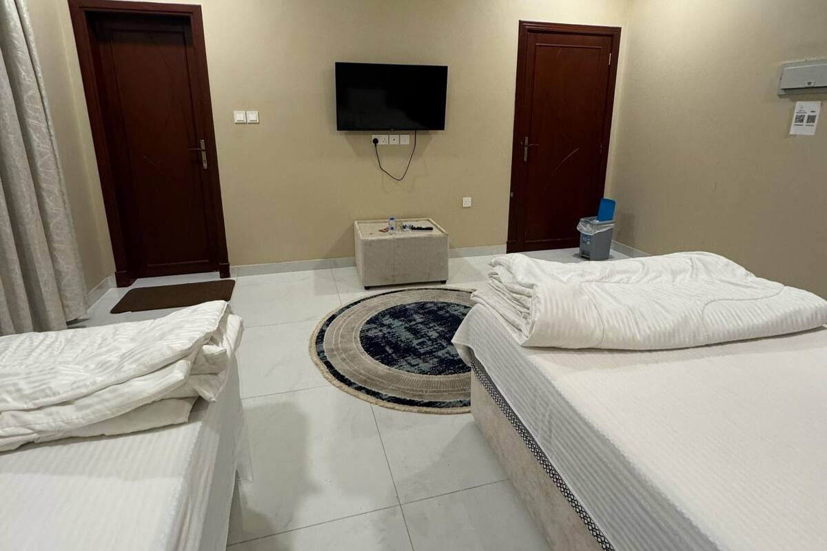 A hotel room with two beds, a TV mounted on the wall, a small table, and a door.