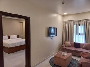 A hotel room with a bed, a sofa, a TV, and a coffee table. - Pyramids Hotel (Seeb)