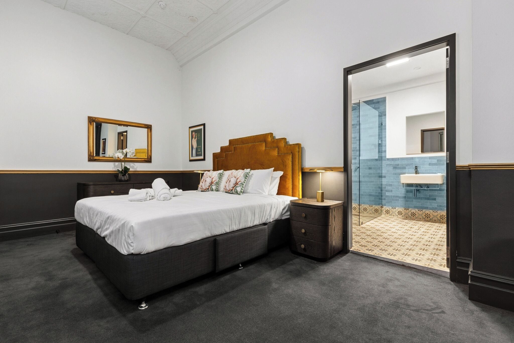 Ein Hotelzimmer mit einem Bett, Nachttischen, einem Spiegel und einem durch eine offene Tür einsehbaren Badezimmer.