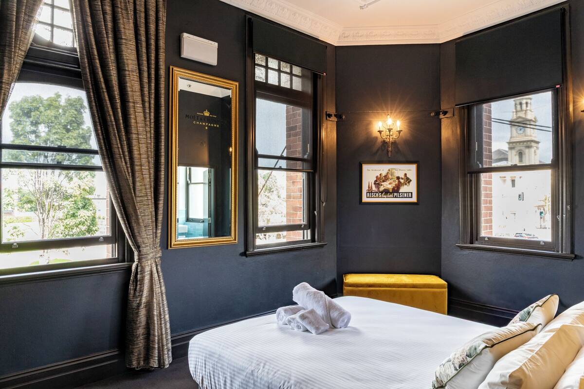 A hotel room with a large bed, a bench, a framed picture, and a window with a view of a building.