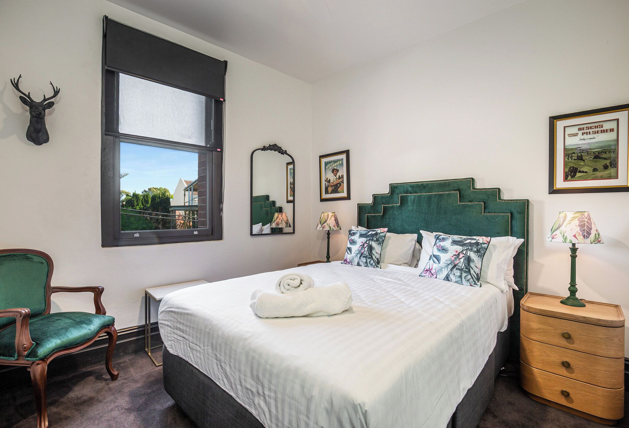 A room with a bed, a chair, a nightstand, a window, and a mirror.