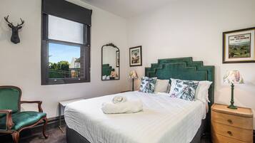 A room with a bed, a chair, a nightstand, a window, and a mirror.