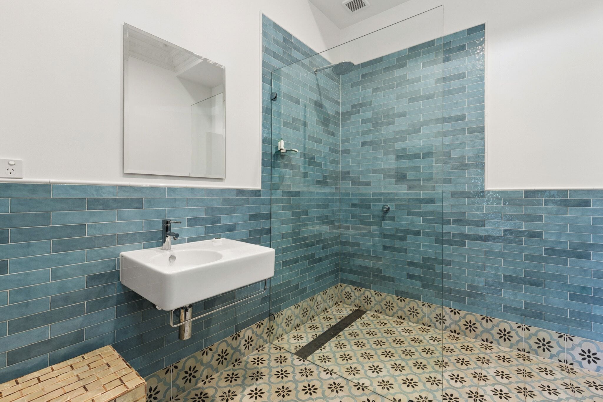 Casa de banho com lavatório branco, cabine de duche em vidro e paredes com azulejos azuis.