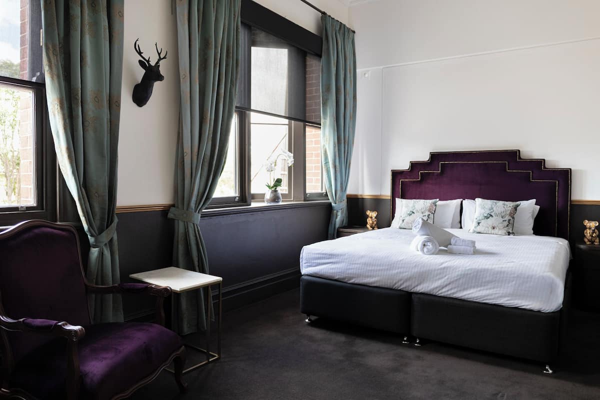A bedroom with a bed, a chair, a window with curtains, and a mounted deer head.