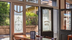 A hotel interior with a wooden table, chairs, and a view of the street outside. - Imperial Hotel Paddington (Paddington)