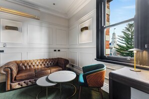 A room with a leather sofa, a round table, a teal chair, and a window with a view of a building. - Imperial Hotel Paddington (Paddington)