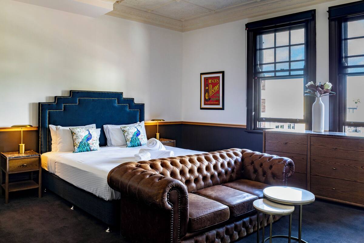 A bedroom with a large bed, a tufted leather sofa, a small round table, and a window with a view.
