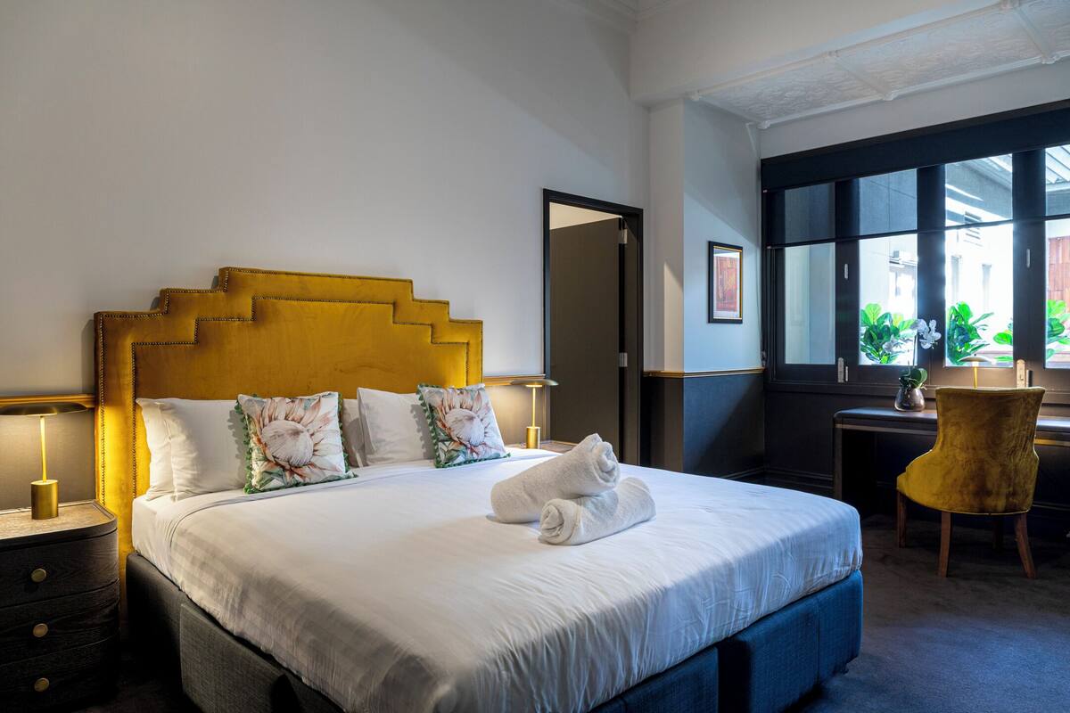 A hotel room with a bed, bedside lamps, a desk, and a chair.