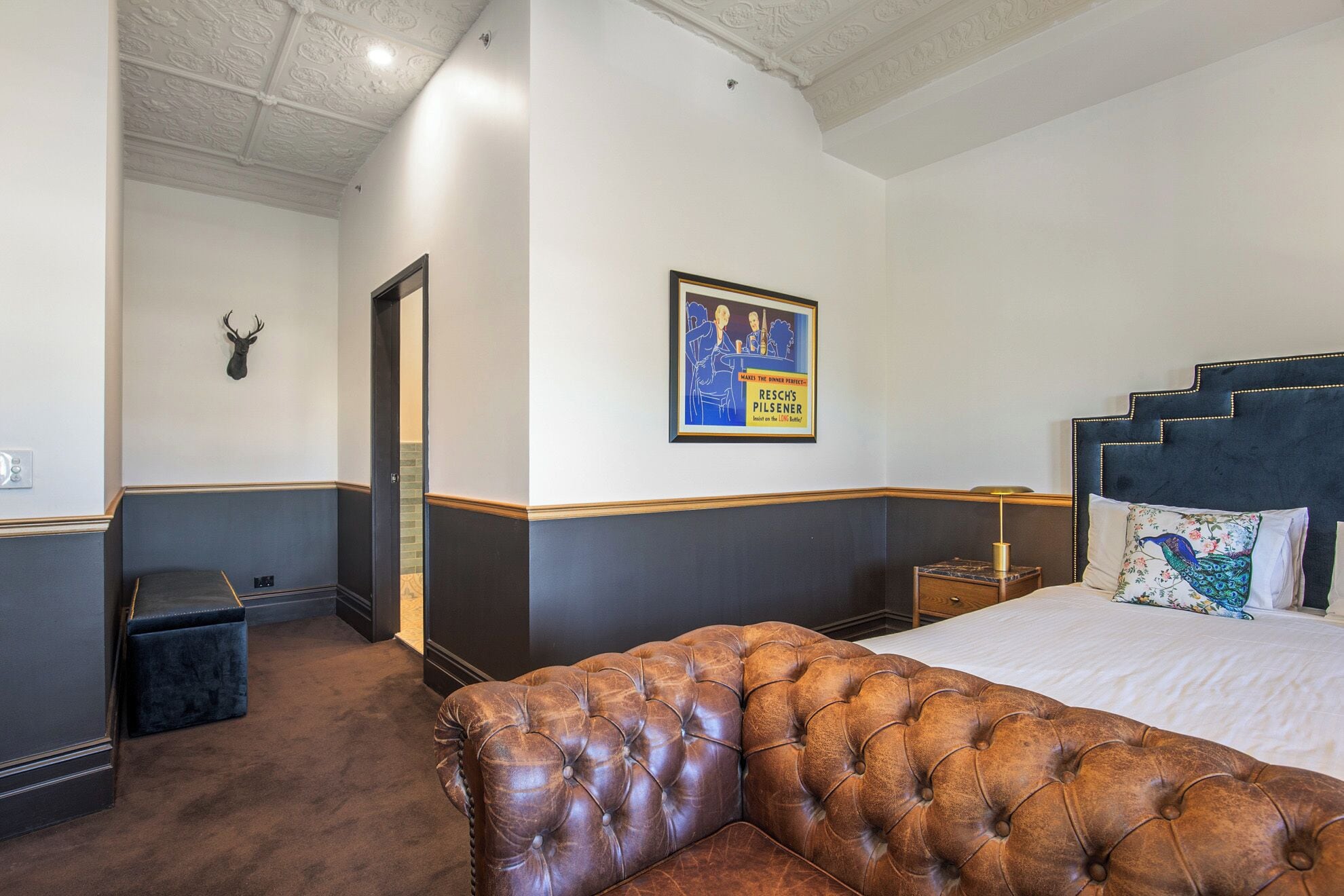 Une chambre d’hôtel avec un grand lit, un canapé en cuir capitonné, une affiche encadrée au mur et une décoration représentant une tête de cerf.