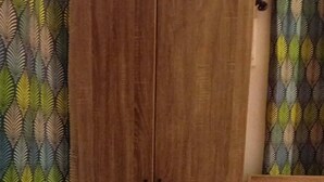 Een slaapkamer met een houten garderobe, een bed met een roze dekbedovertrek en behang met patroon.