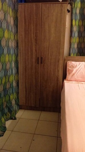 Ein Schlafzimmer mit einem Holzschrank, einem Bett mit rosa Bettdecke und gemusterten VorhÀngen.