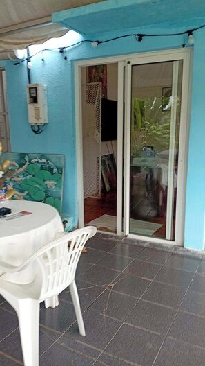 A patio area with a white table and chairs, a power outlet, and a sliding glass door leading to an interior space.