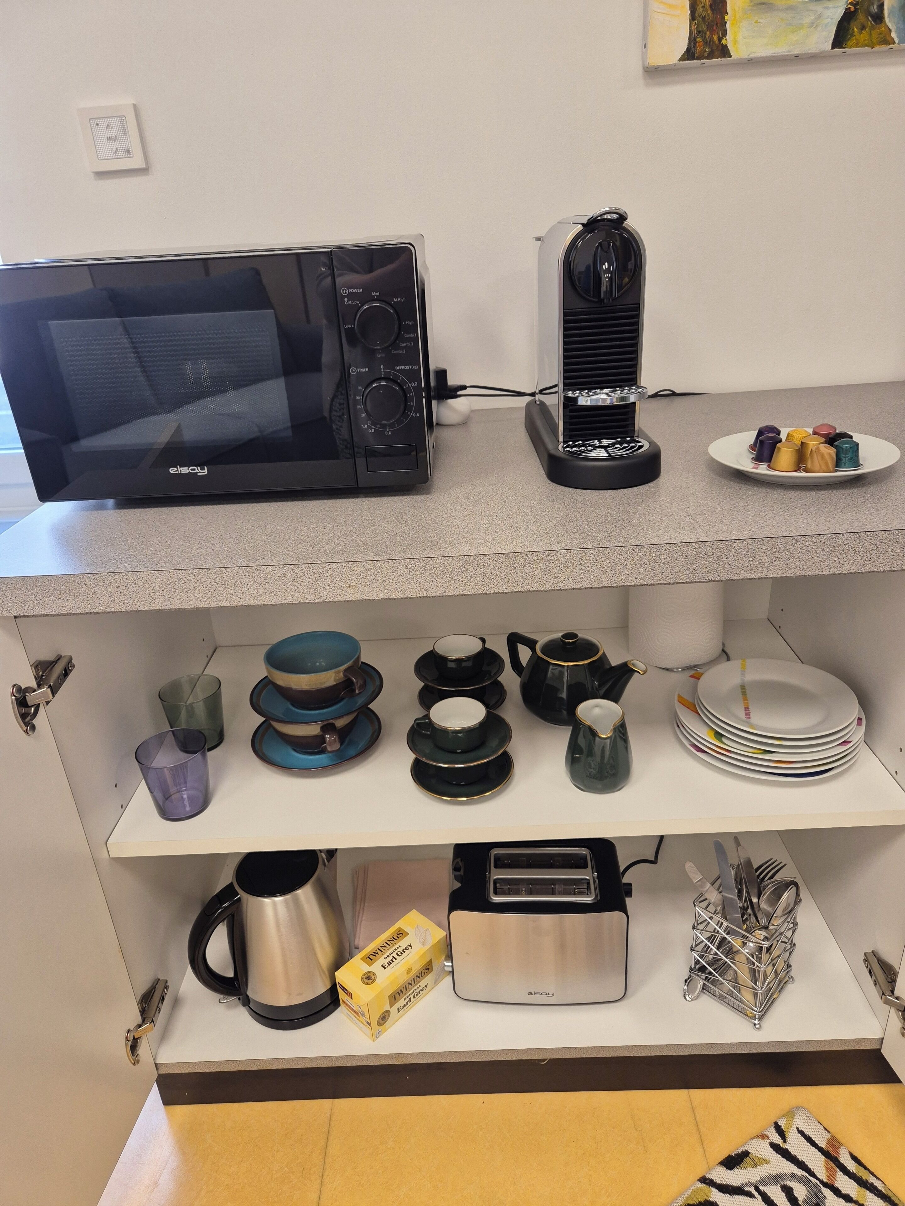 Une cuisine équipée d’un four à micro-ondes, d’un grille-pain et de divers ustensiles de cuisine rangés sur des étagères.