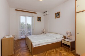 Ein Schlafzimmer mit Bett, Nachttisch, Kommode, Klimaanlage, Fenster mit Vorhängen und einer Tür.