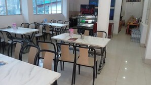 Una sala da pranzo con diversi tavoli e sedie, un frigorifero con bevande e un cartello che segnala la zona cucina.