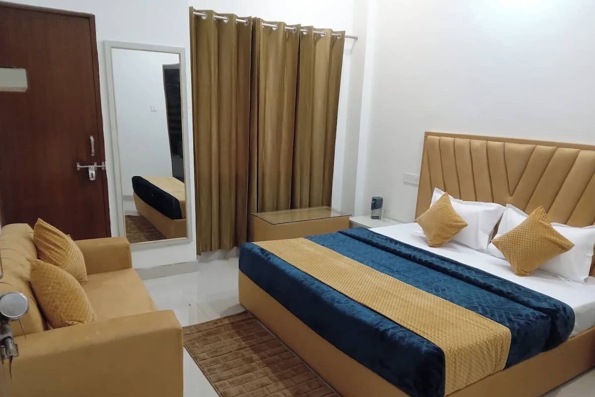 Una habitación de hotel con una cama, un sofá, un espejo y una ventana con cortinas.