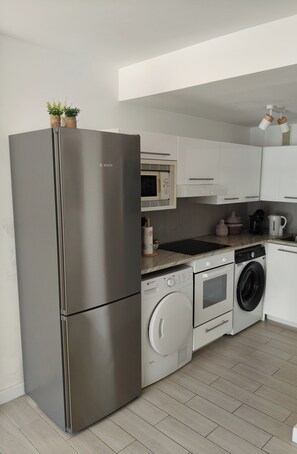Eine moderne Küche mit einem Edelstahl-Kühlschrank, einer Mikrowelle, einer Waschmaschine und einer Kaffeemaschine.