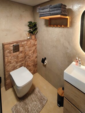 Ein Badezimmer mit Steinwand, Toilette, Waschbecken und Handtuchhalter.