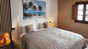 Una camera da letto con un letto, un quadro con palme, una finestra e un lampadario.