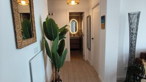 Un corridoio con uno specchio grande, una pianta in vaso, una porta che dà su un bagno e un elemento decorativo a parete.