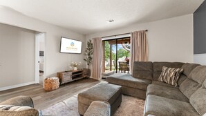 En moderne stue med en modulsofa, et fladskærms-tv og en skydedør, der fører til en udendørs terrasse.