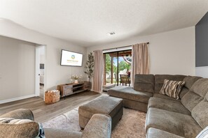A modern living room with a sectional sofa, a flat-screen TV, and a sliding glass door leading to an outdoor patio. - Poolside at The Pointe 2BDR (Branson)