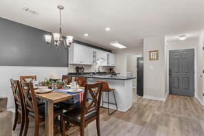 A modern kitchen with white cabinets, a central island, and a dining area with wooden chairs and a table. - Poolside at The Pointe 2BDR (Branson)
