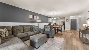 En moderne stue med et gråt sofasæt, et spiseområde og et køkken i baggrunden.