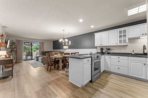 A modern kitchen with white cabinets, a central island, and a dining area with a table and chairs. - Poolside at The Pointe 2BDR (Branson)