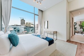 A modern hotel room with a large bed, a desk, a mirror, and a view of the cityscape. - PVH - Signature Livings - 2BR Penthouse (Dubai)