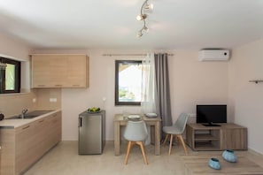 Une cuisine compacte comprenant un réfrigérateur, une table à manger avec des chaises, un téléviseur et une fenêtre avec des rideaux.