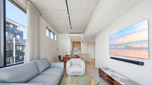 A modern living room with a glass coffee table, a sofa, a dining area with chairs, and a kitchen in the background. - Tranquil 2-bed With Water View (Canberra)