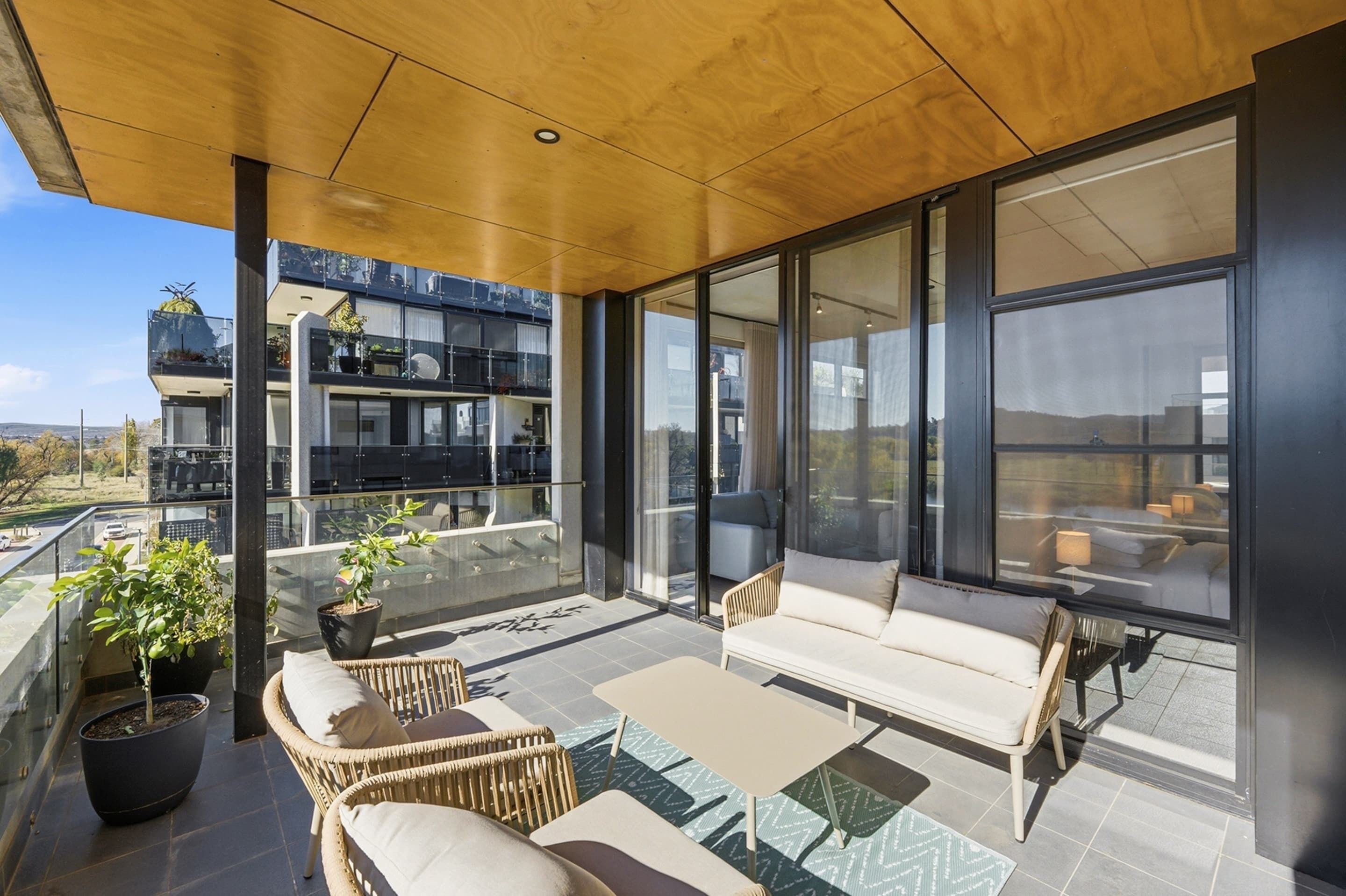 A modern balcony with wicker furniture, potted plants, and a view of a building with balconies and windows.