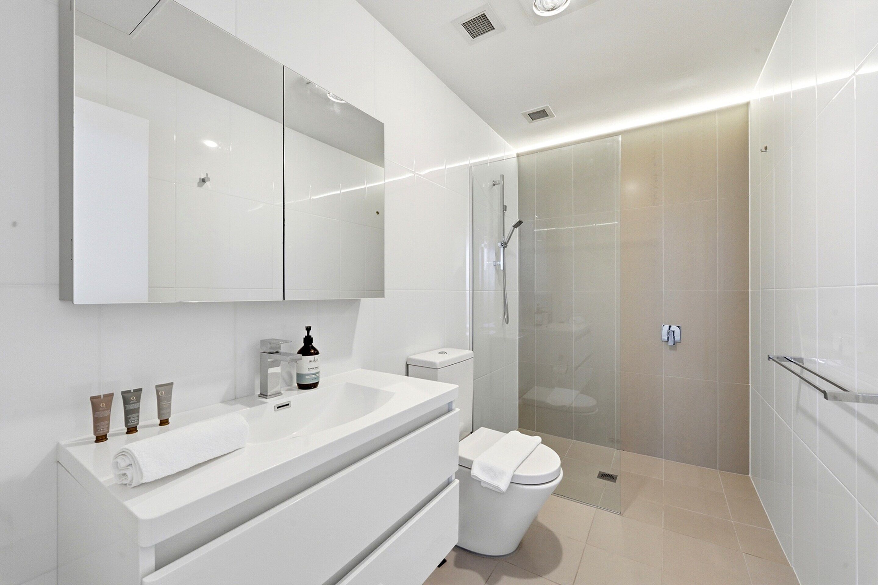 Een moderne badkamer met een witte wastafel, een douchecabine met glazen wanden en een toilet.