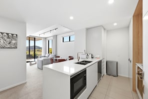 Cozinha moderna com ilha central, área de jantar com sofá e cadeiras, e vista para o exterior.