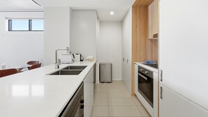 A modern kitchen with white cabinetry, a stainless steel sink, a built-in oven, and a compact trash bin. - Tranquil 2-bed With Water View (Canberra)