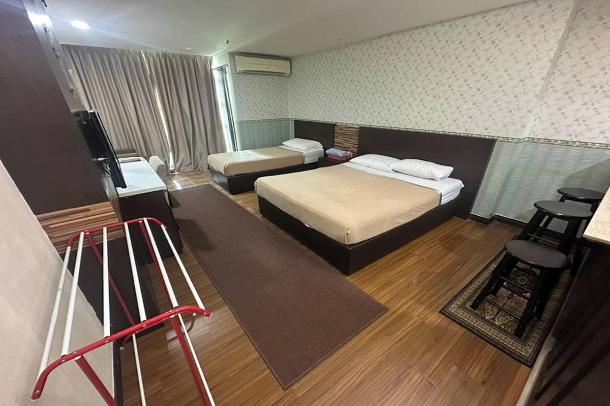 A hotel room with two beds, a desk, a chair, a small table, a window with curtains, and a patterned wall.
