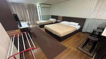 A hotel room with two beds, a desk, a chair, a small table, a window with curtains, and a patterned wall.