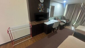 Habitación de hotel con escritorio, silla, sofá, televisión y un reloj en la pared.
