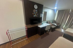 Habitación de hotel con escritorio, silla, sofá, televisión y un reloj en la pared.