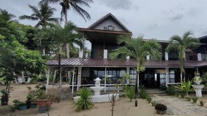 A two-story building with a peaked roof, surrounded by a garden with various plants and a central fountain. - Puerto Paraiso Hostel (Puerto Princesa)