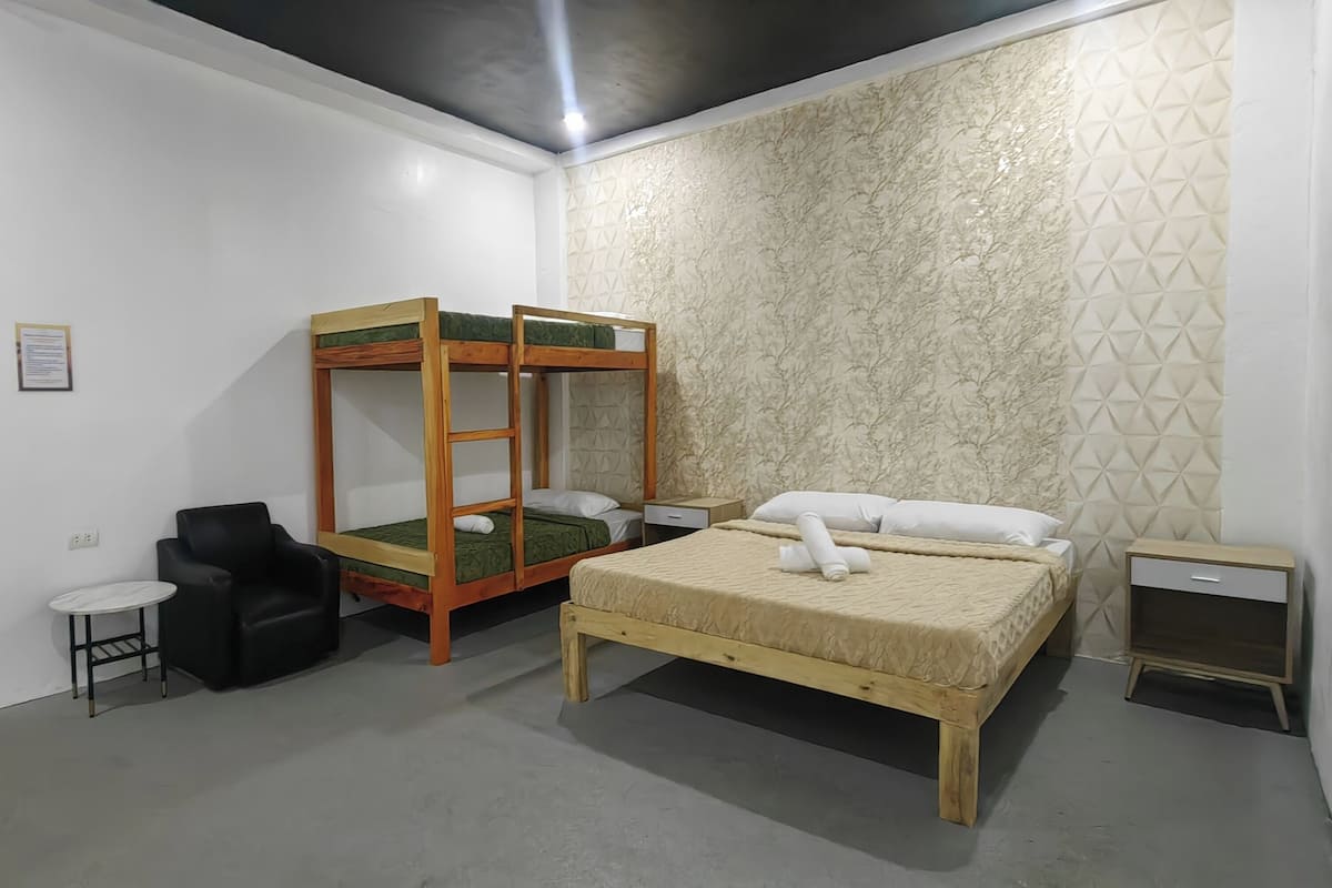 Una habitación con una cama litera, una cama individual, una mesita pequeña, una silla y una mesita de noche.