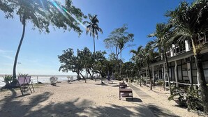 Un hotel frente a la playa con arena dorada, palmeras y cielo despejado.