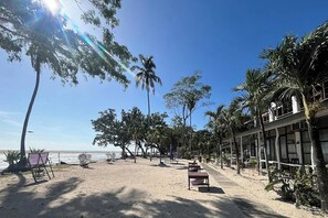 Un hotel frente a la playa con arena dorada, palmeras y cielo despejado.