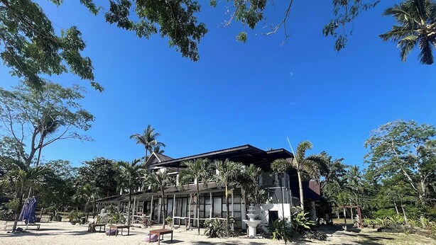 Un edificio de techo inclinado, rodeado de palmeras y otra vegetación.