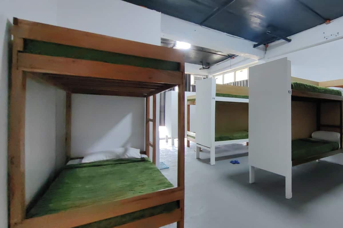Camas literas con ropa de cama verde, paredes blancas y un marco de puerta visible.